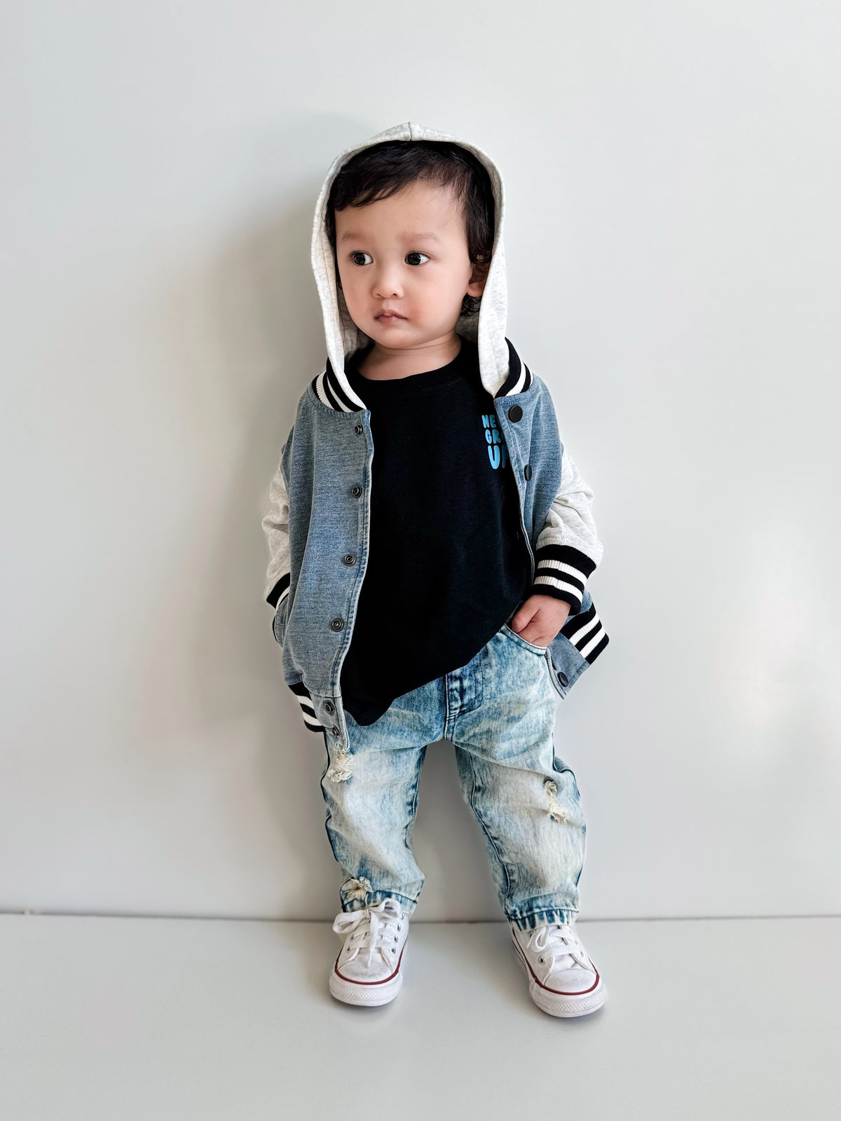 Child wearing a blue denim-look jacket with a hood, black shirt, and light blue jeans on a white background