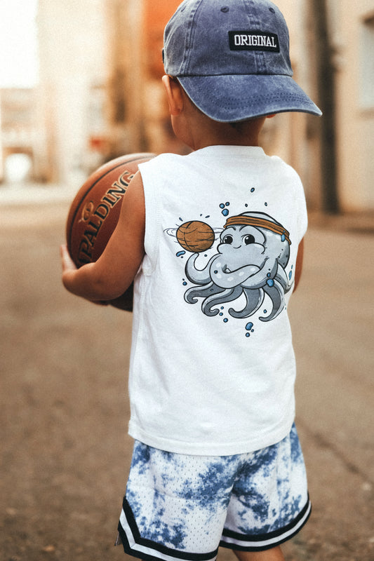 A child wearing a white muscle tank top with a cartoon octopus basketball player graphic, holding a basketball, and a blue baseball cap.